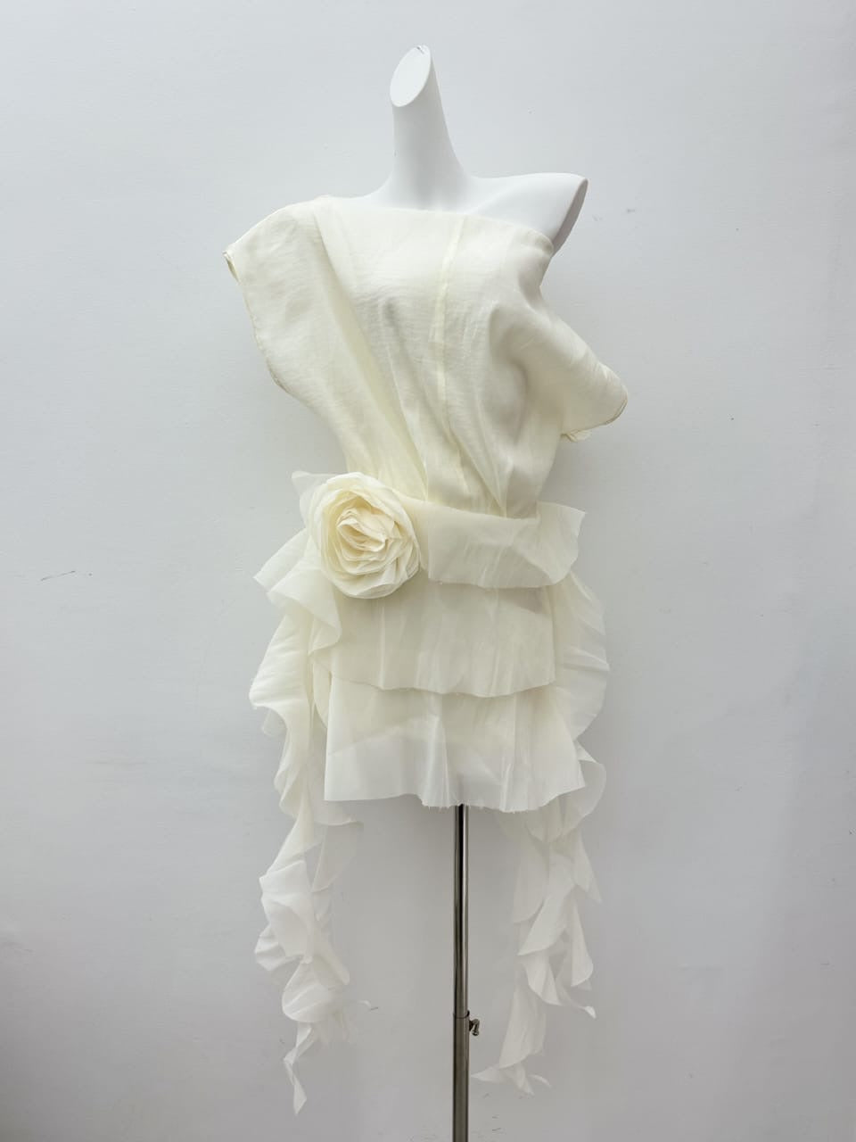 Ivory satin mini dress on mannequin with layered ruffle hem and rosette accent