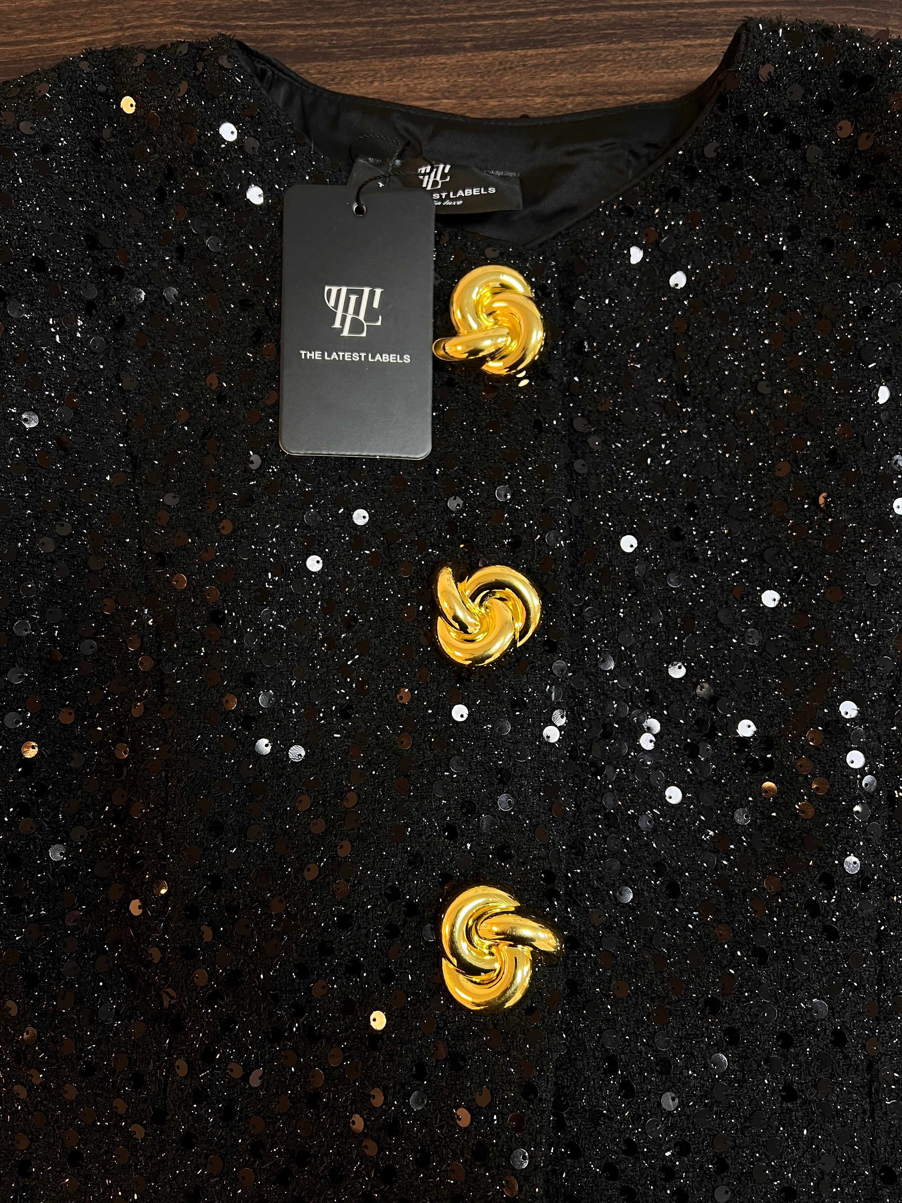 Black sequin top close-up with gold swirl buttons and crew neckline