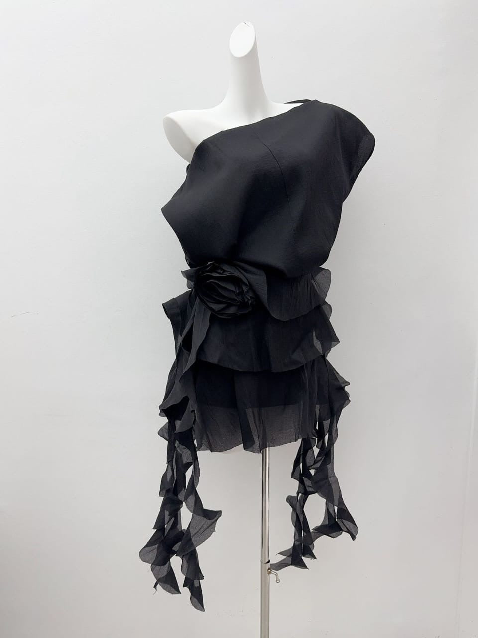Black satin mini dress on mannequin with layered ruffle hem and flower detail