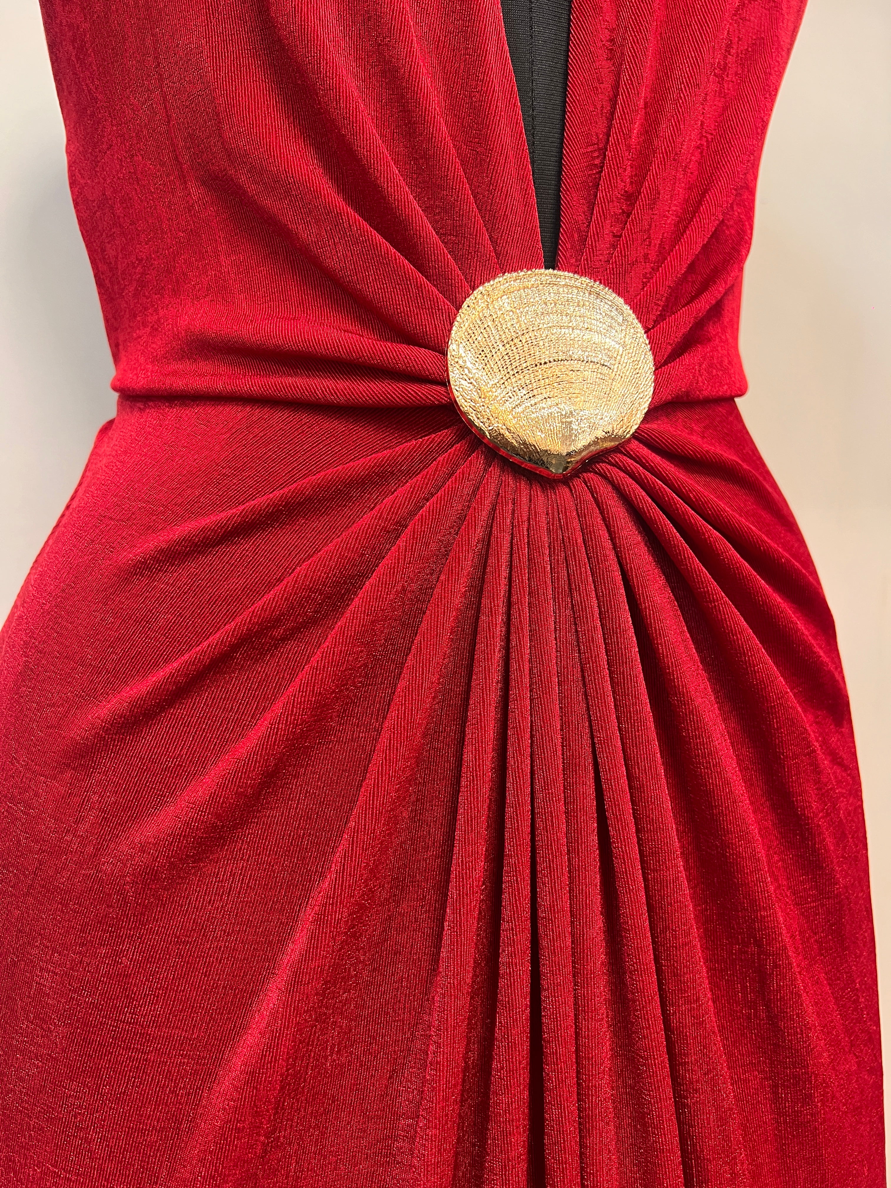 Red gathered halter gown with gold round clasp at waist and fan-like pleats